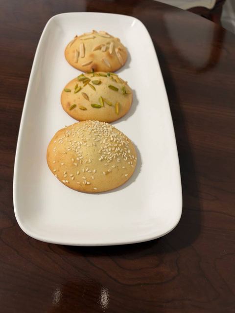 Round cookies with pistachio and sesame toppings on an oblong white platter