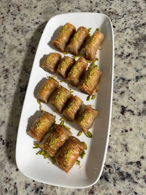 Rows of pistachio baklava rolls on a long white platter, seen from above