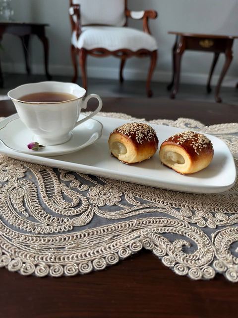 Sesame buns and a cup of tea served on a lace placemat at the dining table